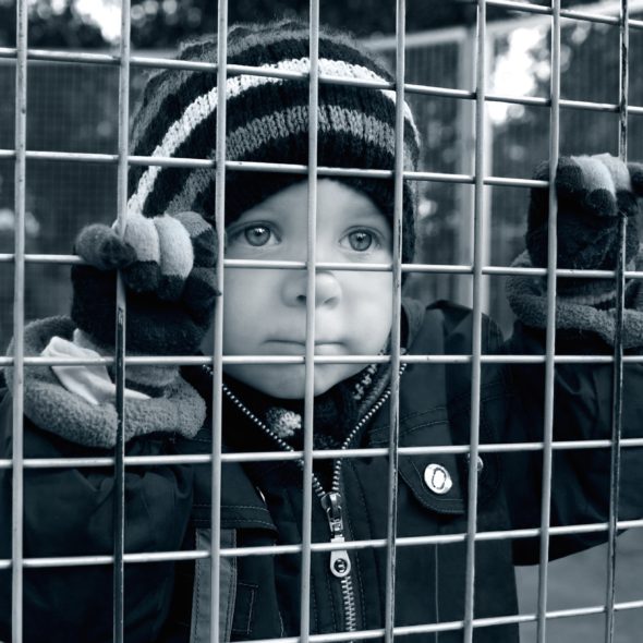 CHILD LOOKING THROUGH FENCE