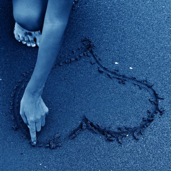 HAND MAKING HEART IN BLUE SAND